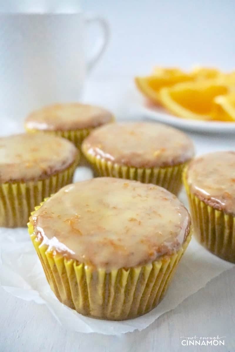  side view of healthy orange poppy seed muffins with vanilla glaze on white parchment paper