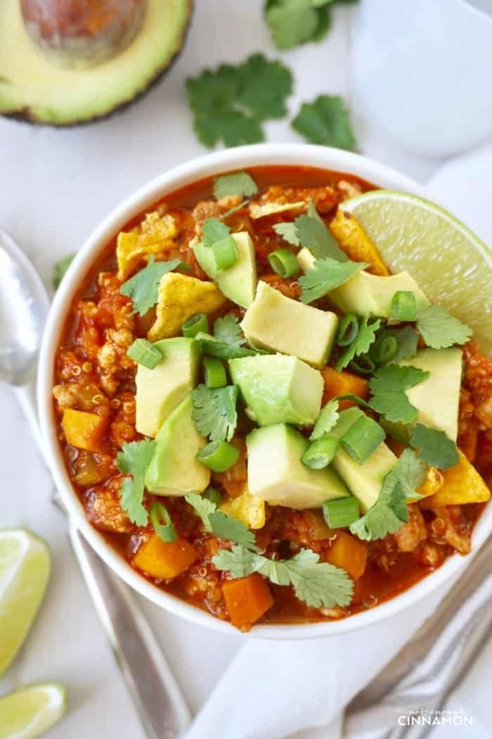 overhead shot of quinoa turkey sweet potato chili served in a white bowl topped with avocado and cilantro