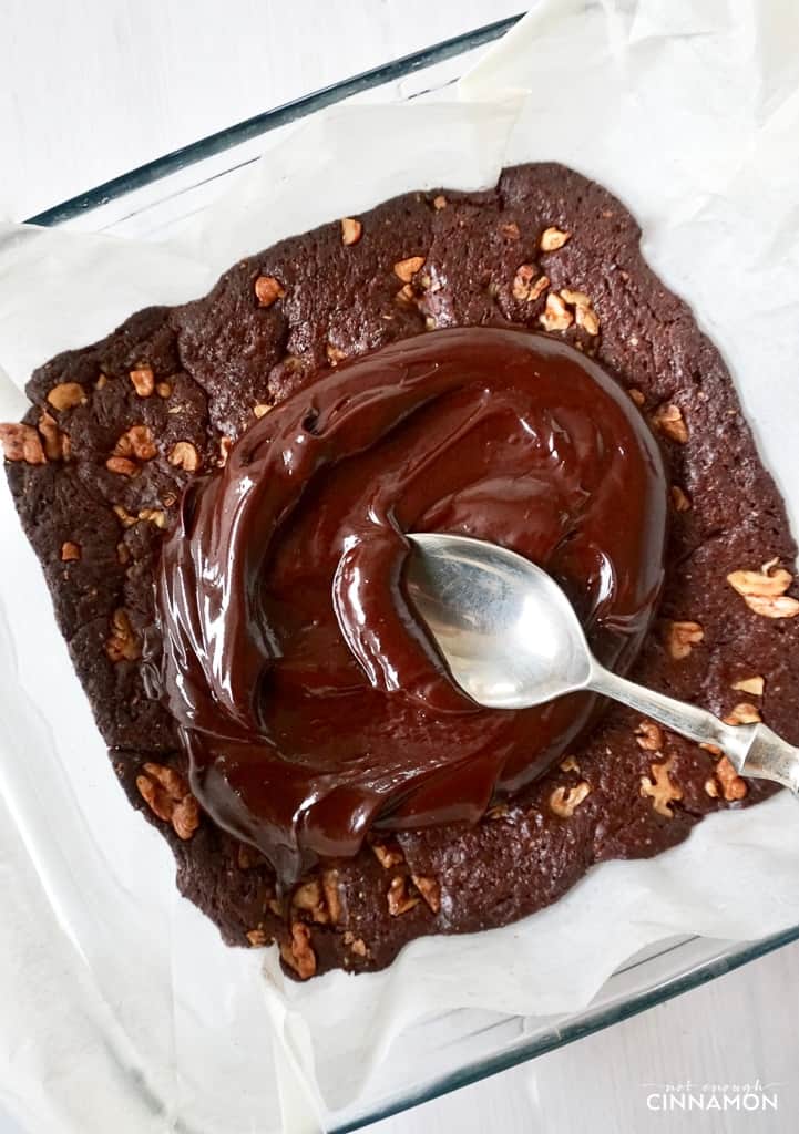 coconut cream chocolate frosting being spooned on top of paleo chocolate brownie in a pyrex baking dish