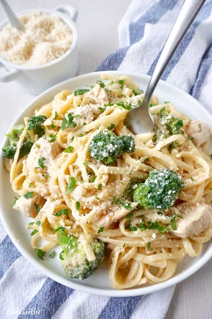 a plate of chicken and broccoli fettucine with cauliflower alfredo sauce with a dish of parmesan on the side