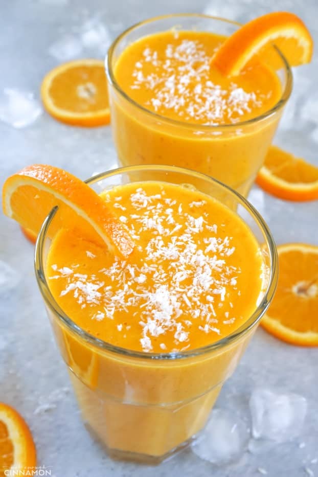 Two glasses of sunshine smoothies, topped with coconut and surrounded by orange slices