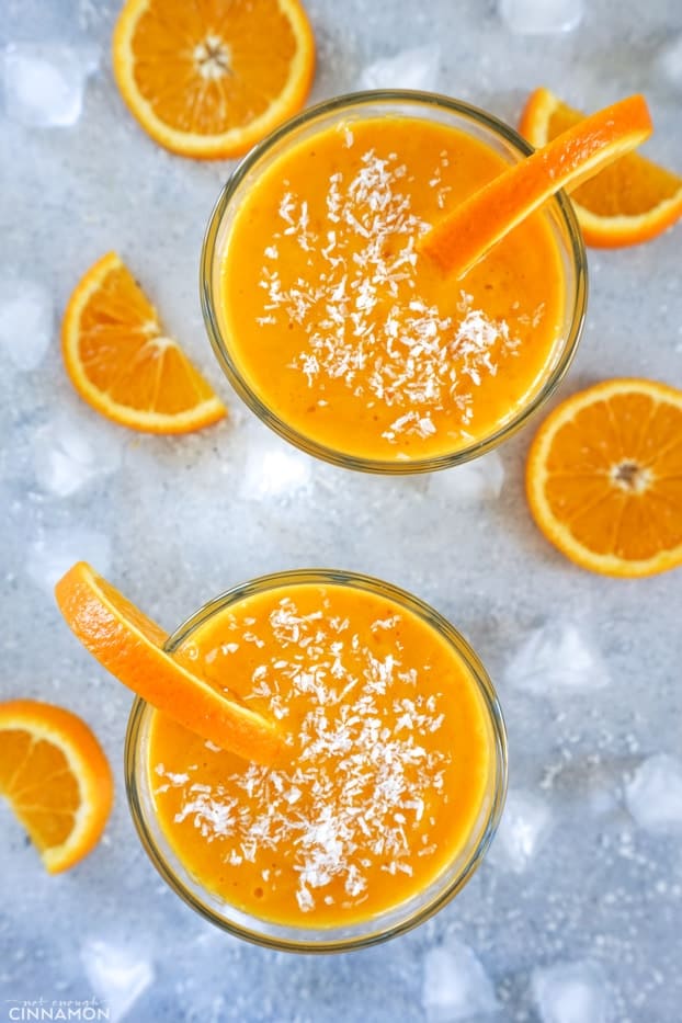 Overhead shot of two smoothie glasses with slices of oranges and ice cubes