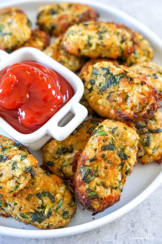 A plate of zucchini tots with a container of ketchup in the middle.