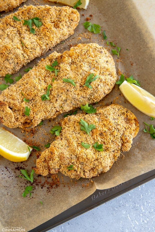 Chicken schnitzel on a baking tray with lemon wedges and parsley