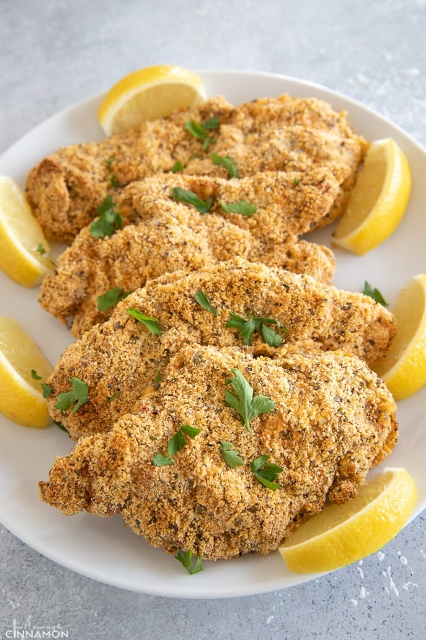 Baked chicken schnitzel in a white plate with lemon wedges and parsley