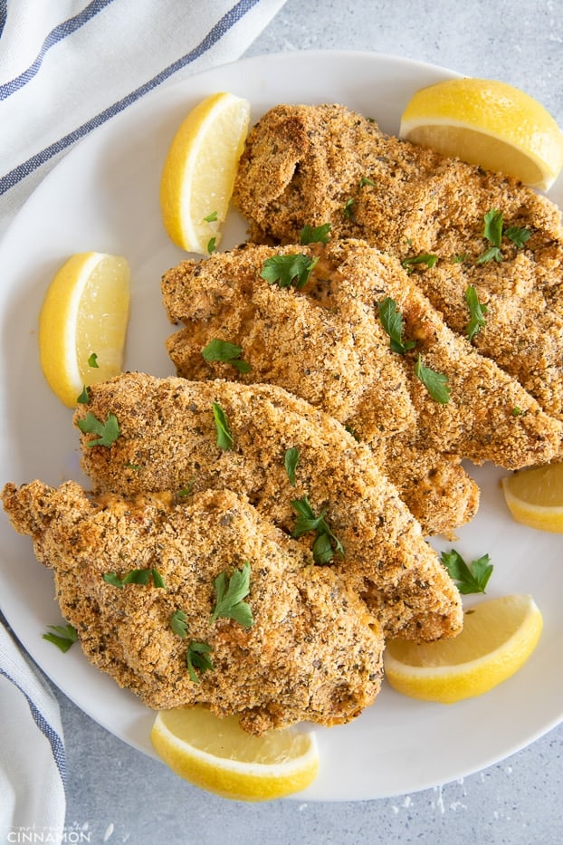 Four chicken schnitzel on a white plate with lemon slices