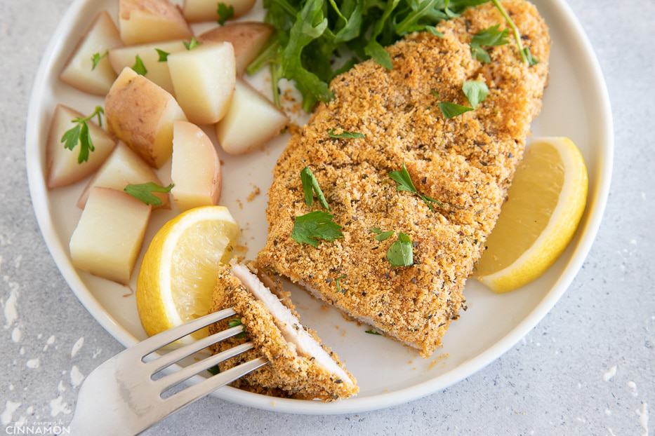 A piece of chicken schnitzel cut in a plate with potatoes and salad