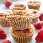 Two strawberry muffins stacked on top of each other, with fresh strawberries around.