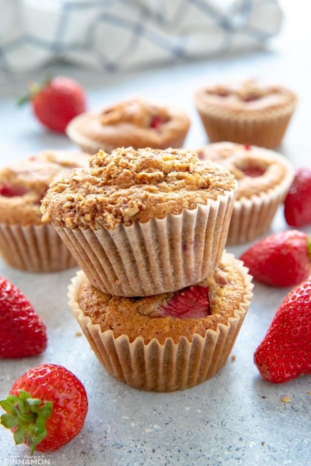 Two strawberry muffins stacked on top of each other, with fresh strawberries around.