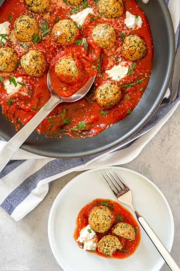 Zucchini meatballs in a skillet with a large serving spoon, next to a white plate with more zucchini meatballs