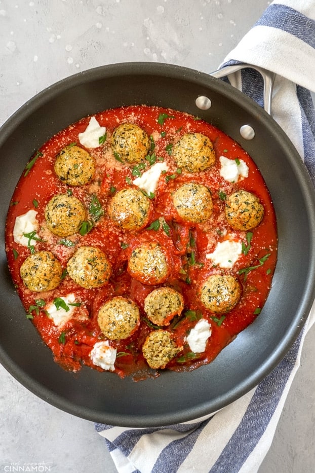 A skillet of baked zucchini meatballs in marinara sauce with ricotta and spinach
