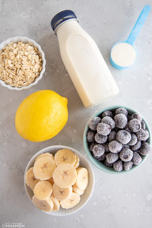 Ingredients for lemon blueberry smoothie: frozen banana and blueberries, oats, a lemon, some milk and protein powder