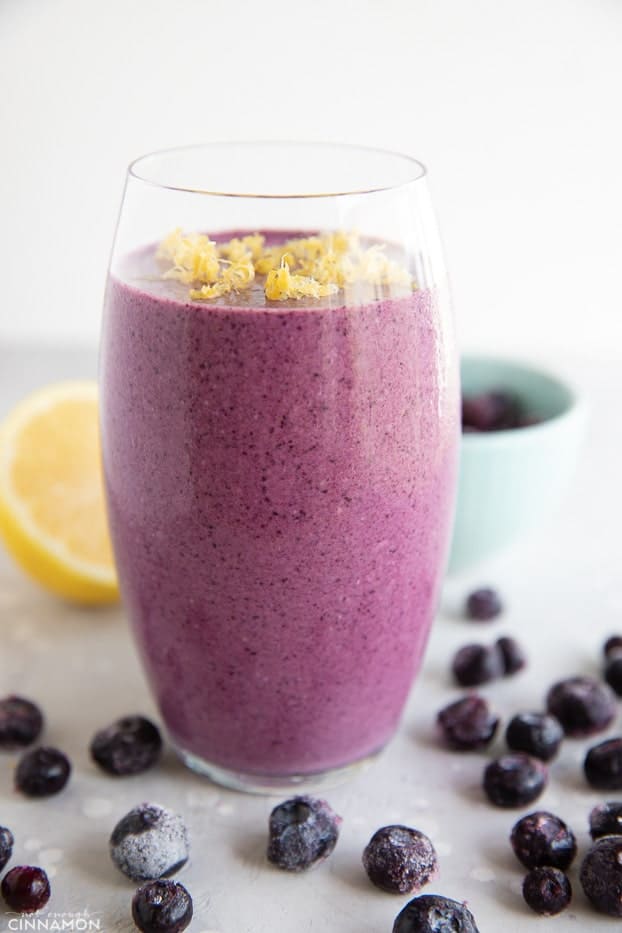Tall glass of blueberry smoothie with frozen blueberries and half a lemon