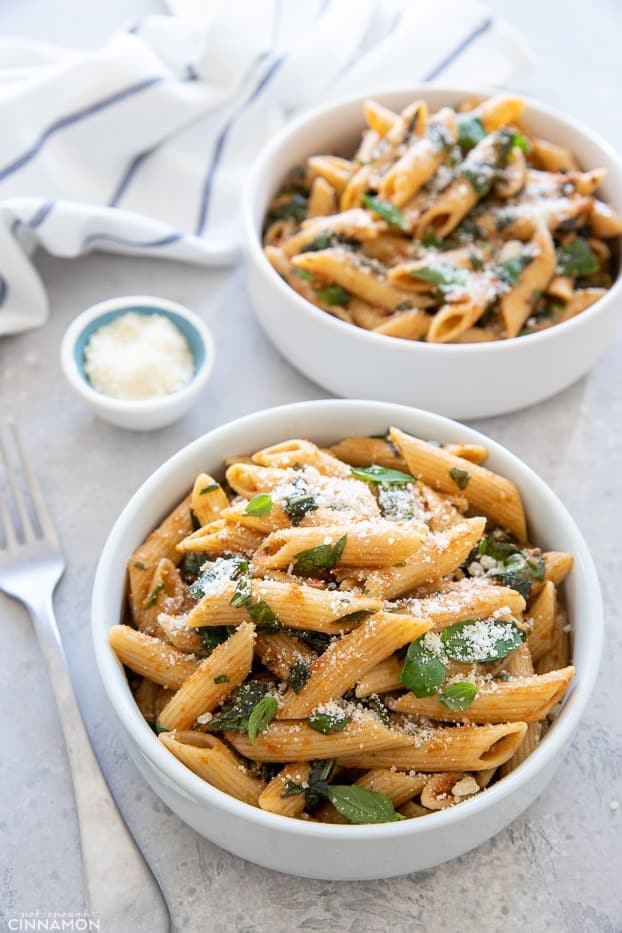 overhead shot of two small bowls with sun-dried tomato pasta with spinach, basil and parmesan cheese
