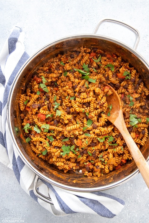 overhead shot of a big pot with healthy one pot taco pasta with a wooden spoon in the pot and a striped kitchen towel on the side