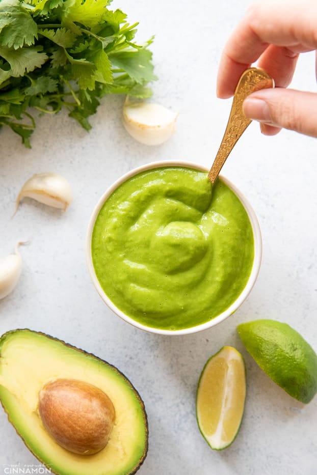 overhead shot of a small bowl with creamy cilantro avocado lime sauce with a golden spoon