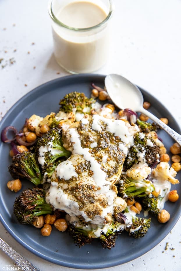 overhead shot of a serving of za'atar spiced sheet pan chicken dinner with roasted vegetables, chickpeas and drizzled with tahini sauce