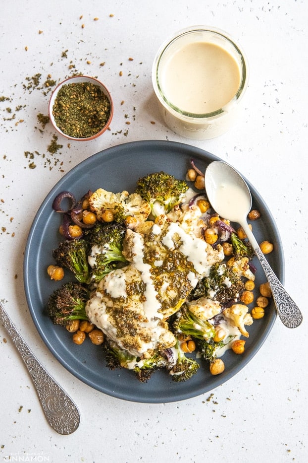 za'atar spiced baked chicken thighs with broccoli, cauliflower and roasted chickpeas on a plate served with a drizzle of tahini sauce