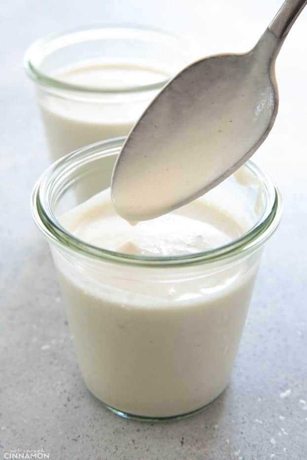 a silver spoon being dipped into a small glass with homemade vegan cashew cream 