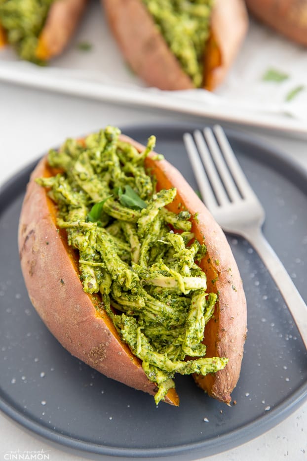 a paleo pesto chicken stuffed baked sweet potato on a black plate with a fork 