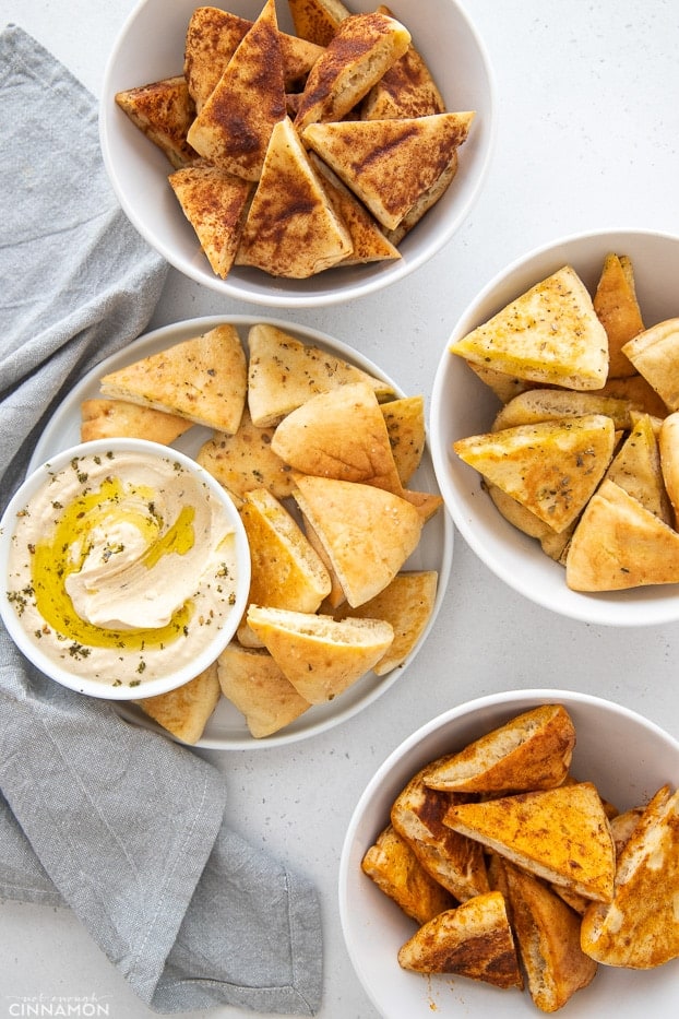 overhead shot of 4 different flavors of homemade Stacy's Baked Pita Chips with a small bowl of hummus