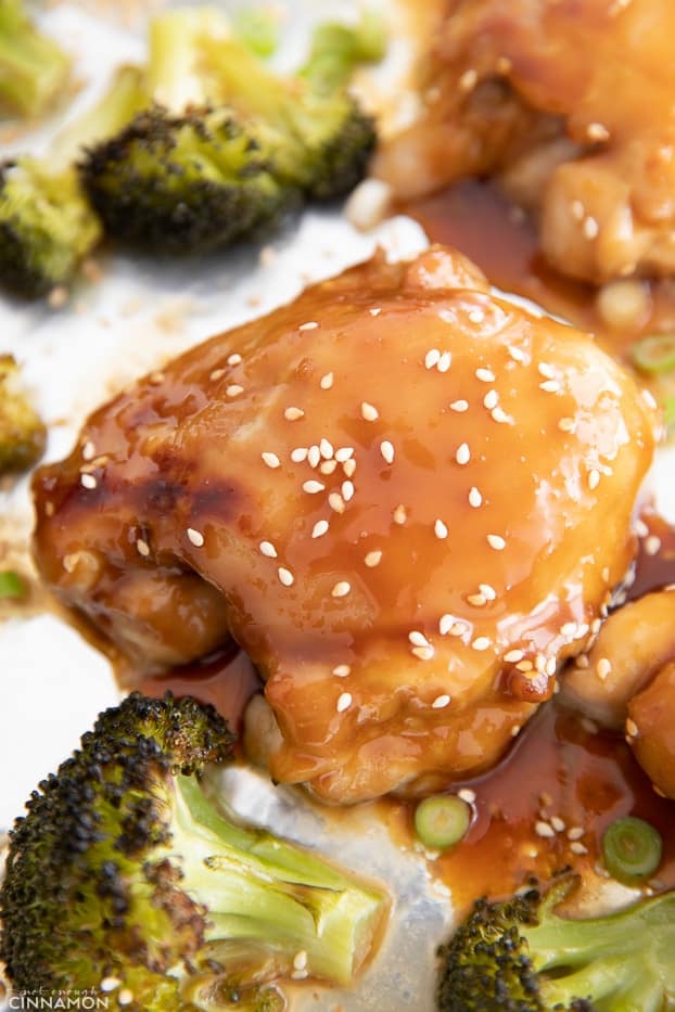 close-up of an oven-baked teriyaki chicken thigh surrounded by broccoli on a sheet pan