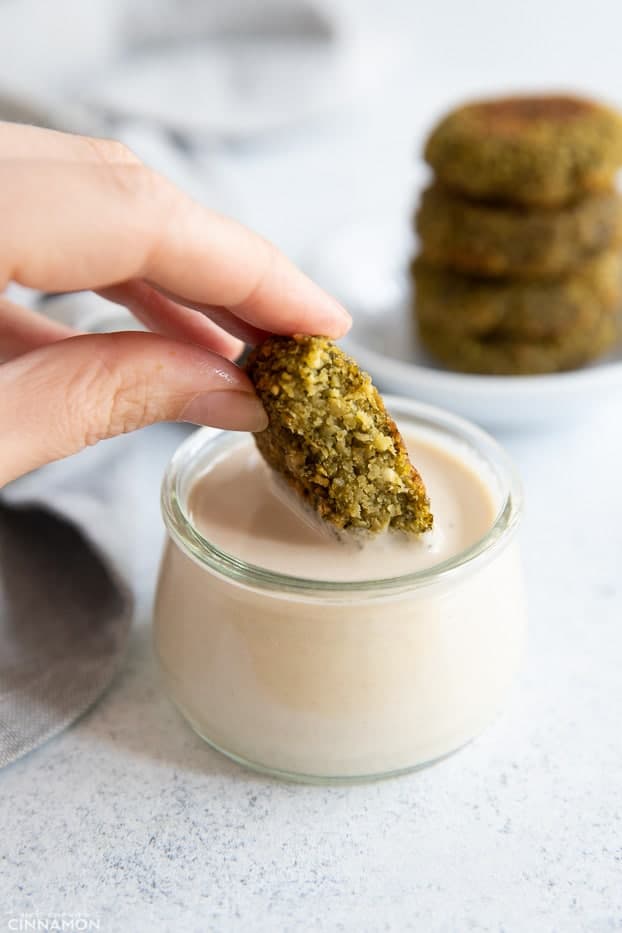 baked falafel a baked falafel patty being dipped into a small glass jar of homemade tahini sauce