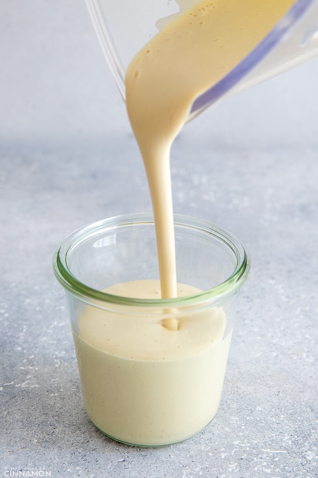 vegan cashew alfredo sauce being poured into a small glass jar 