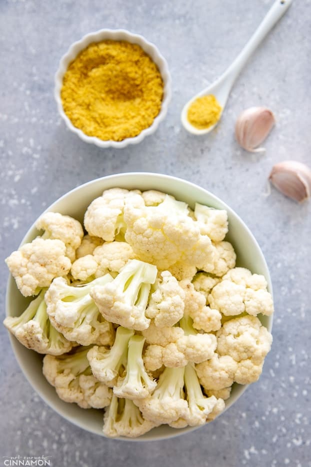 overhead shot of cauliflower florets, nutritional yeast and garlic on a kitchen counter