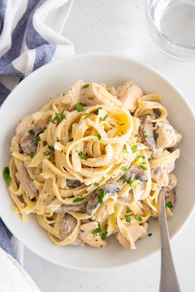 overhead shot of a white bowl with fettuccine Alfredo pasta with chicken and mushrooms