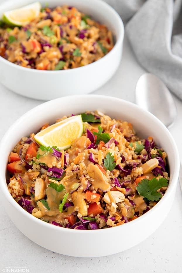 side view of a bowl with Asian Quinoa Salad with chopped veggies drizzled with a creamy Thai Peanut Dressing