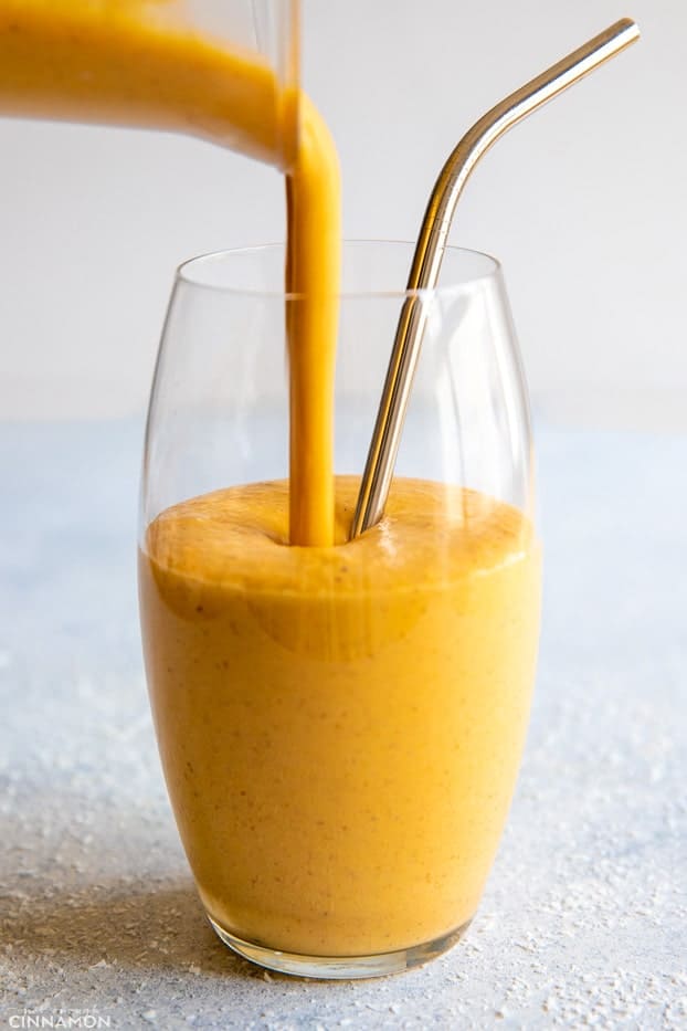 healthy carrot cake smoothie being poured from the Vitamix into a tall drinking glass 