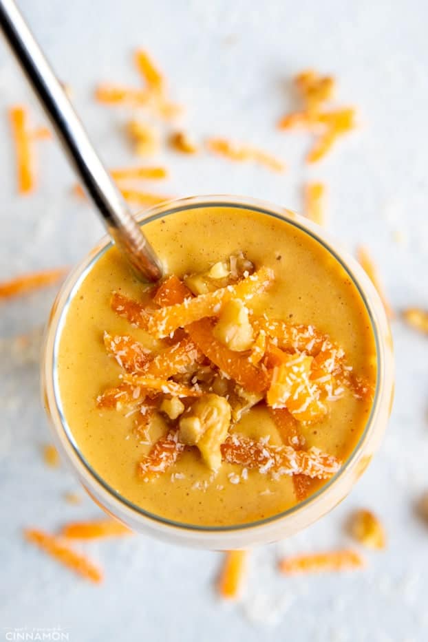 overhead shot of a glass of healthy carrot cake smoothie topped with carrots, chopped nuts and coconut 