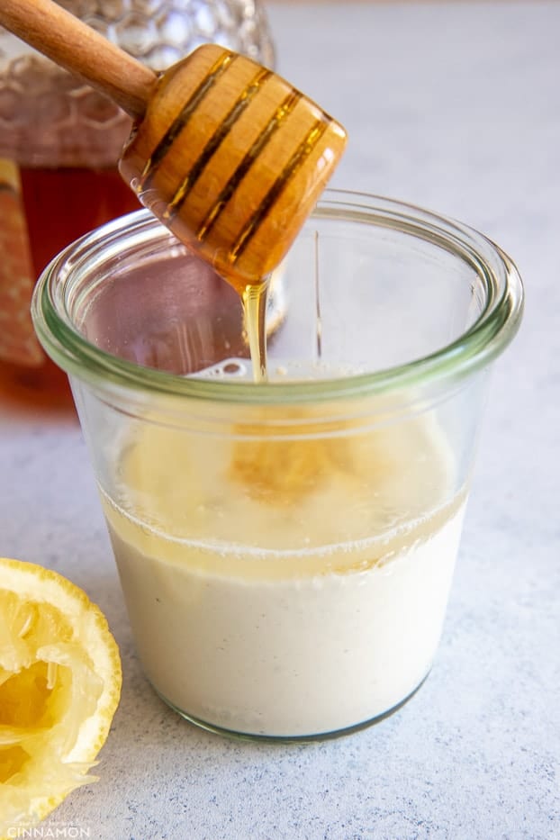 honey being drizzled into a small jar with yogurt and lemon juice to make salad dressing