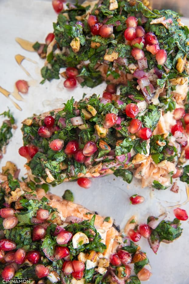 salmon baked in parchment paper being topped with chopped herbs, pomegranate seeds and molasses