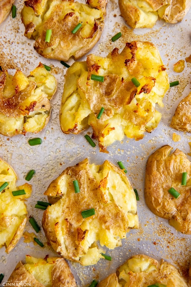 overhead shot of a baking sheet with crispy baked smashed potatoes sprinkled with chives 