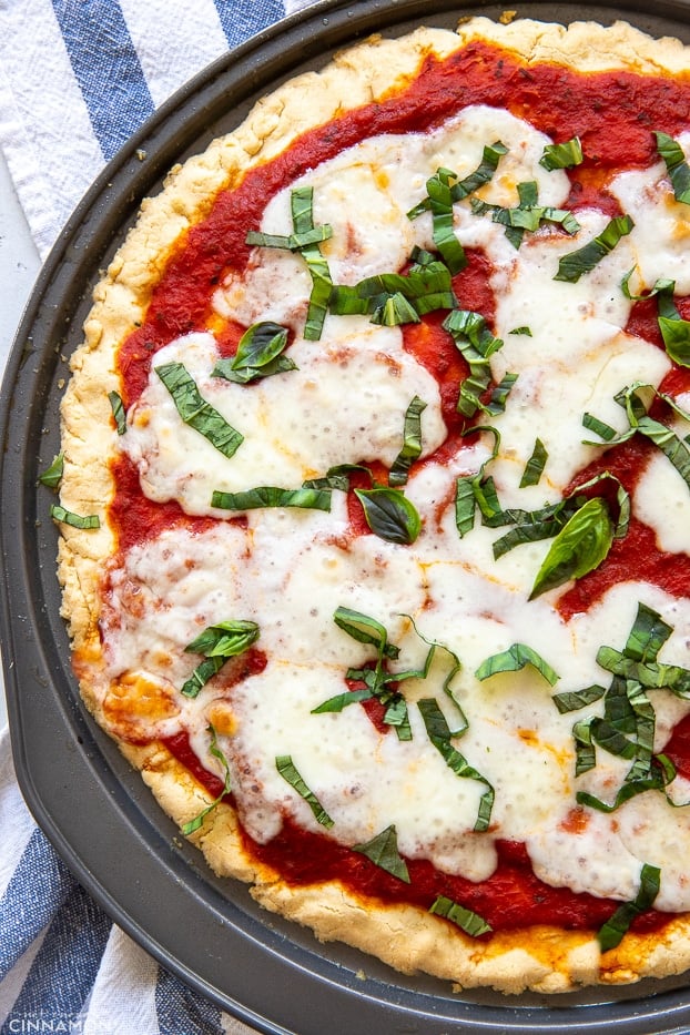 overhead shot of a healthy paleo almond flour pizza crust topped with marinara sauce and basil