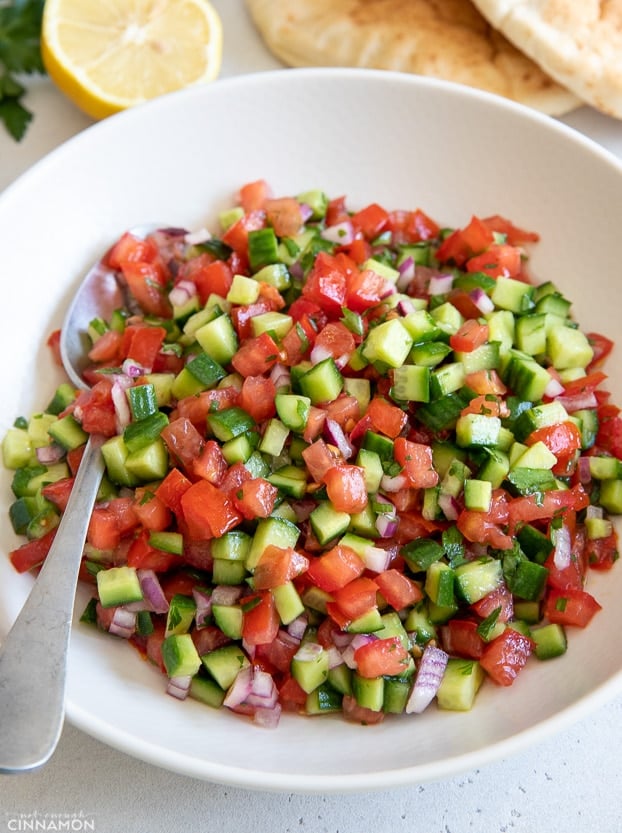 side view of a plate of chopped Israeli salad with a spoon on the side 