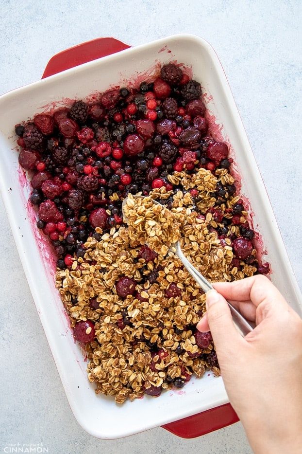 oatmeal crumb topping being sprinkled on top of berry filling 