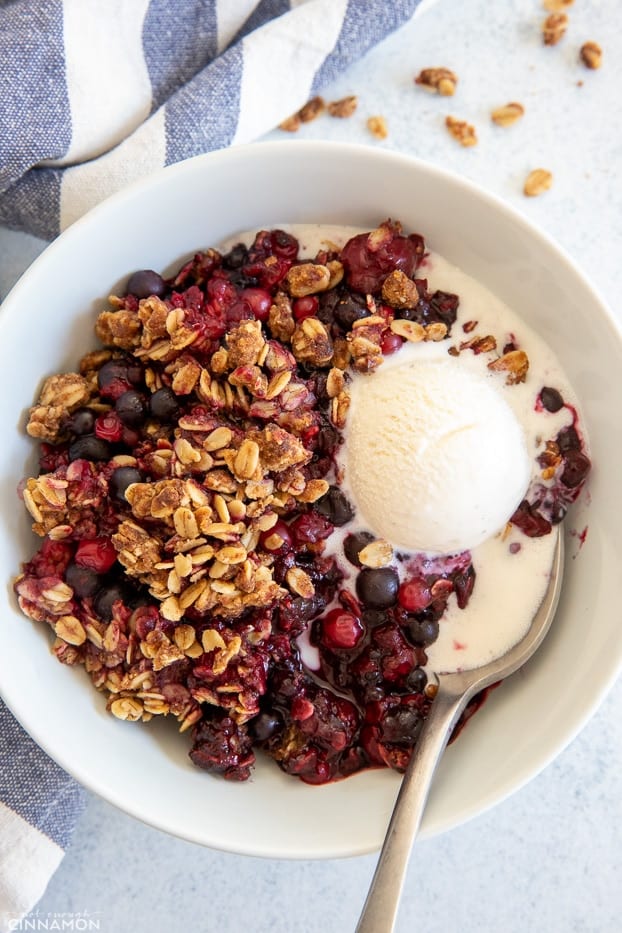 overhead shot of a bowl of berry crisp with a spoon and a bowl of vanilla ice cream 