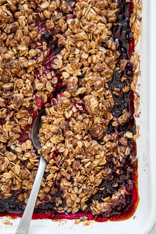 overhead shot of a casserole with healthy berry crisp in a white casserole dish with a silver spoon 