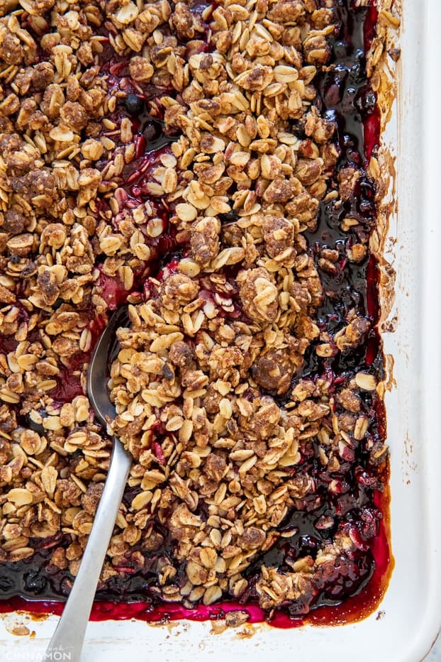 overhead shot of a casserole with healthy berry crisp in a white casserole dish with a silver spoon 