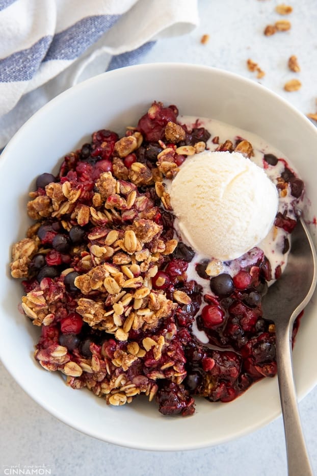a serving of healthy refined sugar-free mixed berry crisp with oatmeal crumble topping and a scoop of ice cream