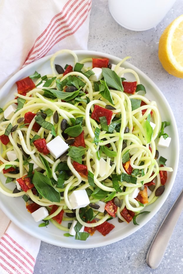 overhead shot of spiralized zucchini salad with goat cheese, sundried tomatoes and fresh herbs 