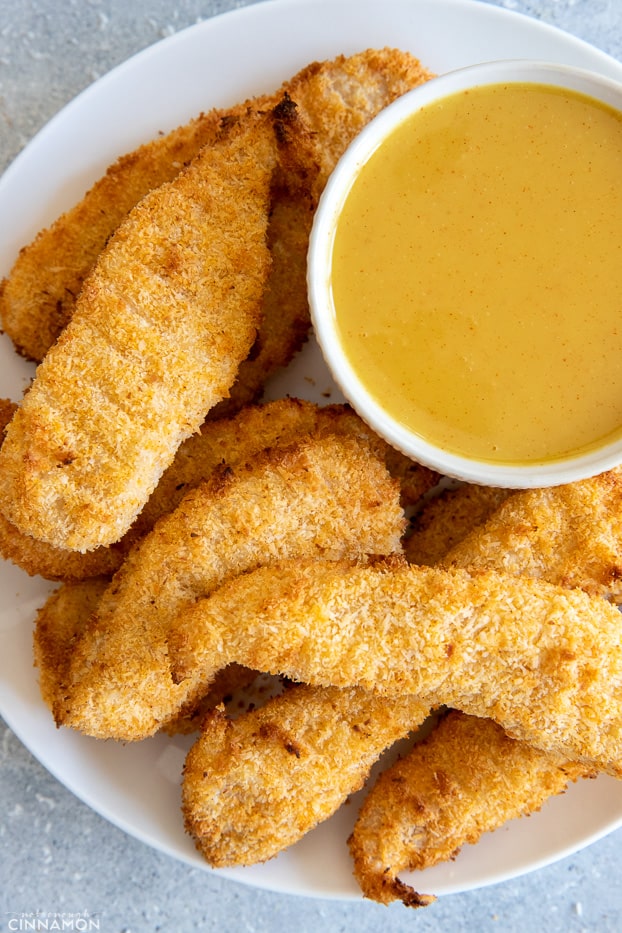 a plate with baked coconut crusted chicken tenders served with a honey mustard dipping sauce