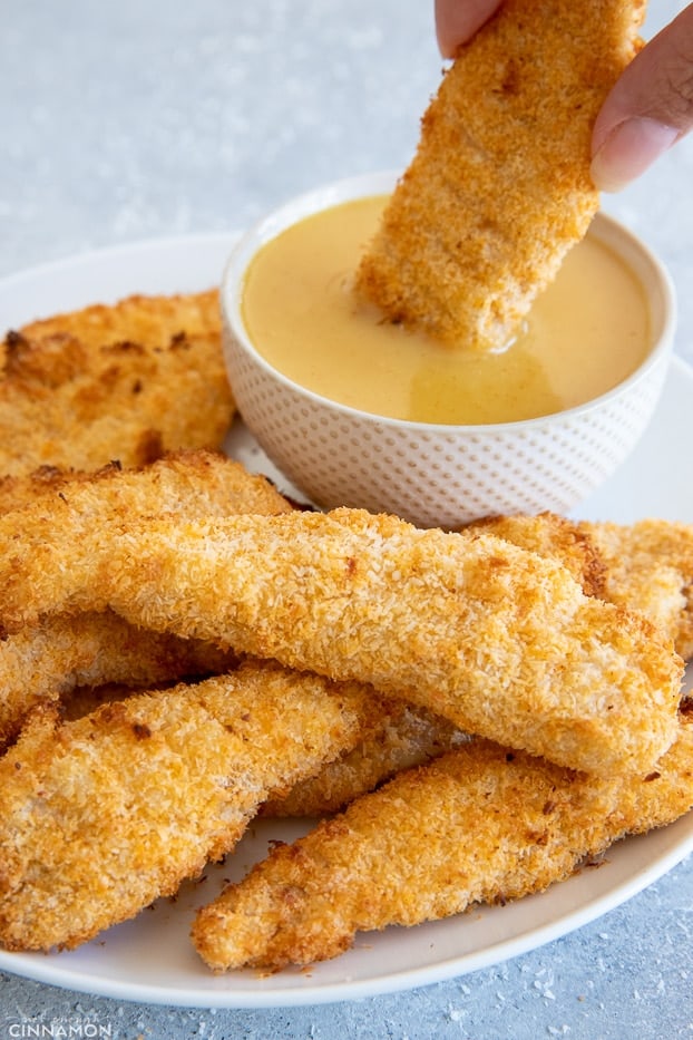 a healthy baked coconut crusted chicken tender being dipped into honey mustard sauce