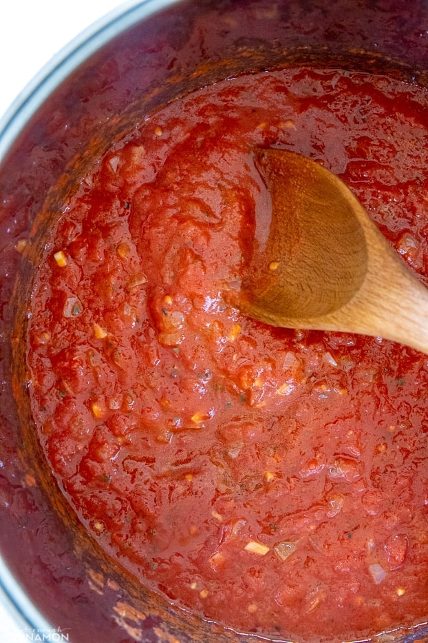 overhead shot of a pot of marinara sauce with a wooden spoon 