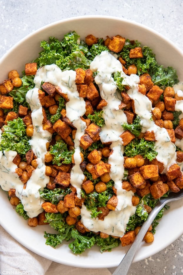 overhead shot of roasted chickpea kale and sweet potato salad drizzled with creamy Greek yoghurt dressing