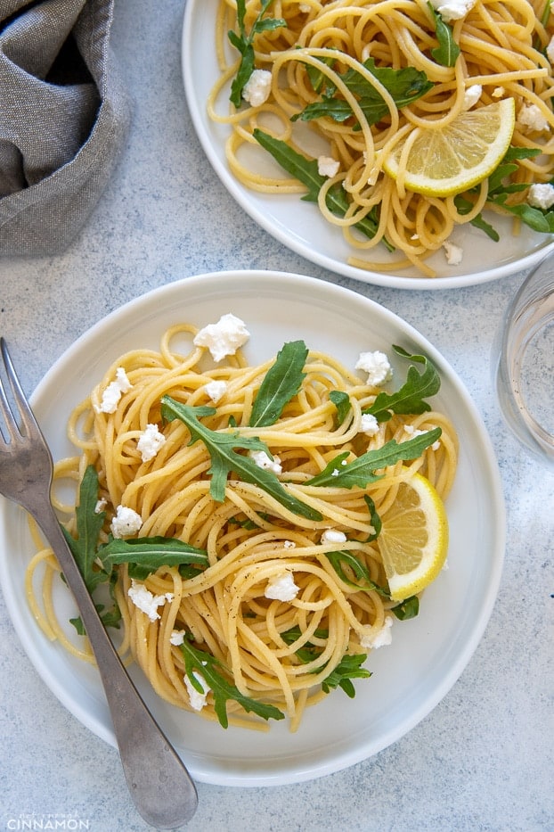 overhead shot of two plates of easy lemon pasta with arugula and crumbled feta