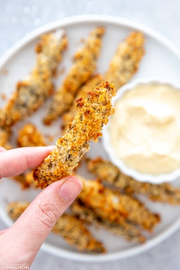 a hand holding a healthy baked portobello mushroom fry over a plate